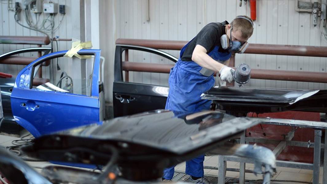 Сотрудник цеха кузовного ремонта наносит краску на поверхность детали автомобиля