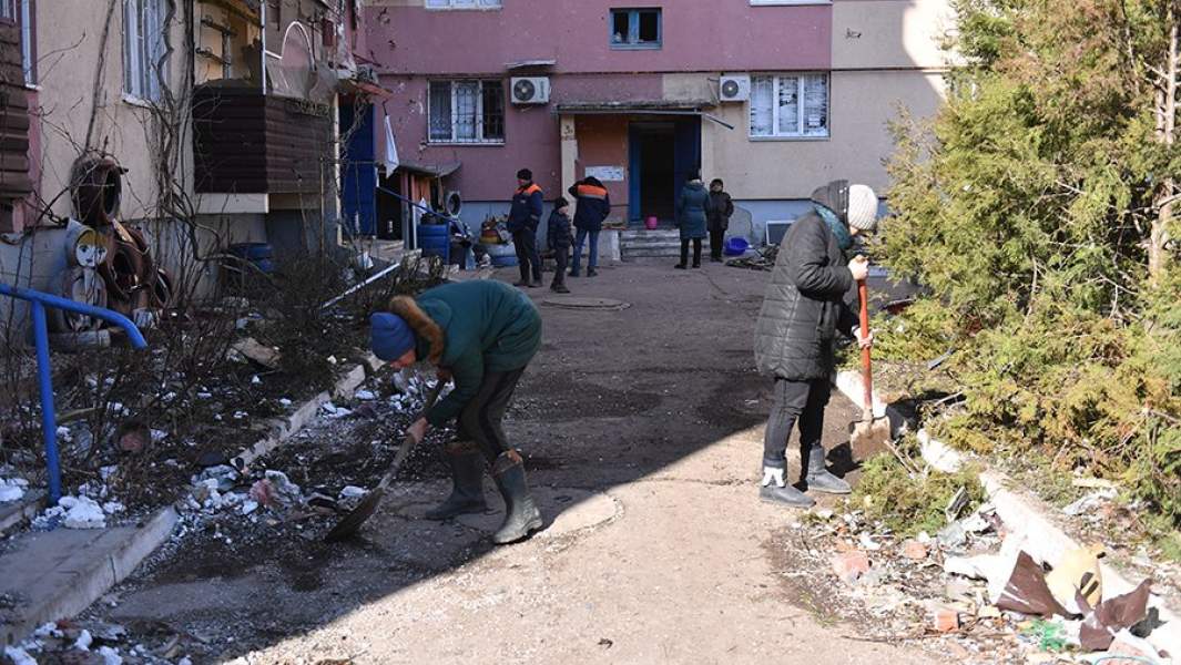 Местные жители убирают мусор во дворе жилого дома, поврежденного в результате обстрела в Волновахе