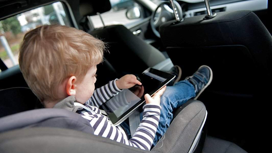 ребенок играет в планшет в детском автомобильном кресле