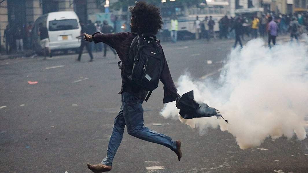 Протестующий откидывает гранату со слезоточивым газом к полицейскому кордону, 9 июля 2022 года