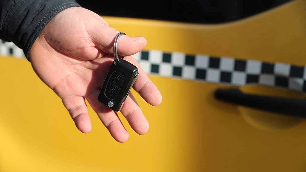 таксист держит ключи от такси напротив своего авто