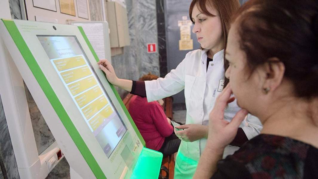 Сотрудница городской поликлиники помогает пациентке оформить талон на прием к врачу