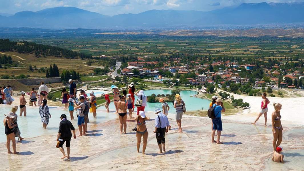 Туристы в травертинах, природных известковых бассейнах, находящихся в природном объекте Памуккале на юго-западе Турции