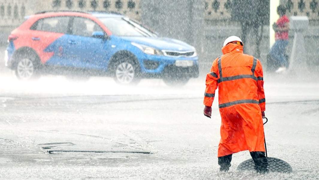 Сотрудник коммунальных служб открывает люк сточной канализации на улице во время ливня в Москве