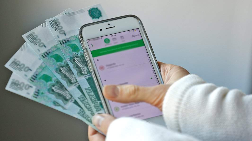 человек держит в руках телефон с электронными средствами и физические деньги