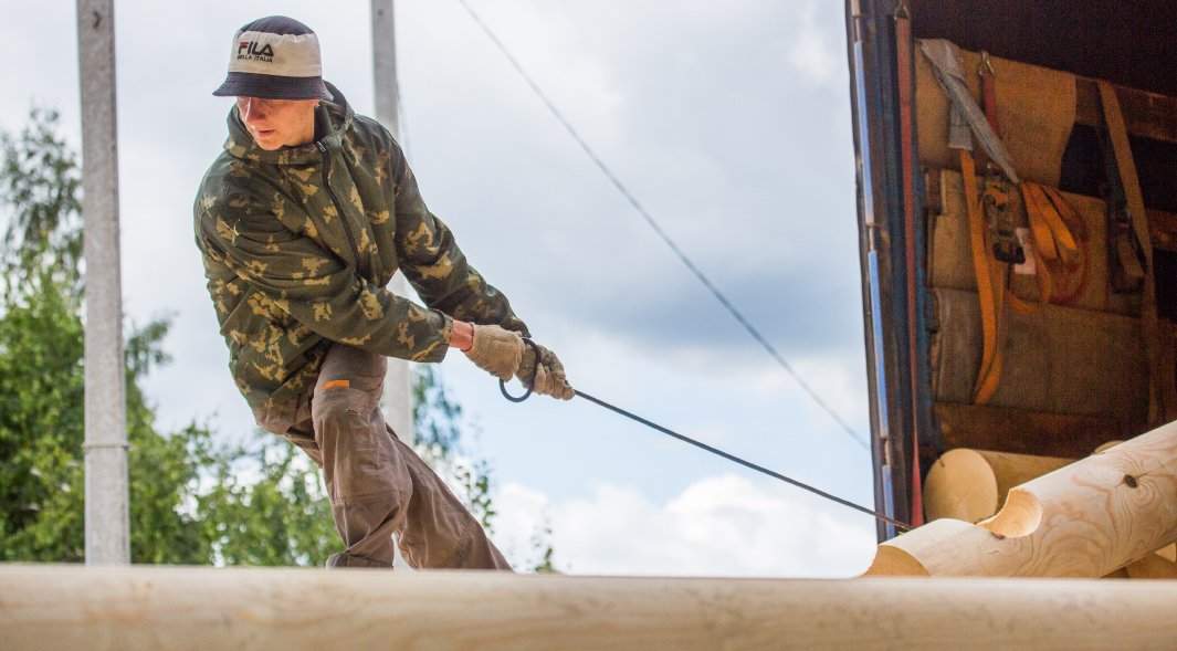 рабочий вытаскивает бревна из грузового автомобиля