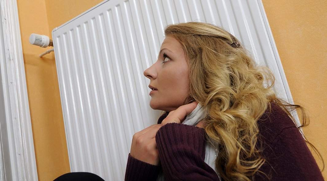 замерзшая девушка прижимается к батарее