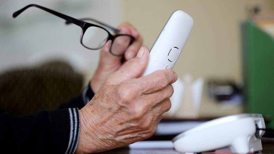 Руки пожилой женщины держат телефон и очки