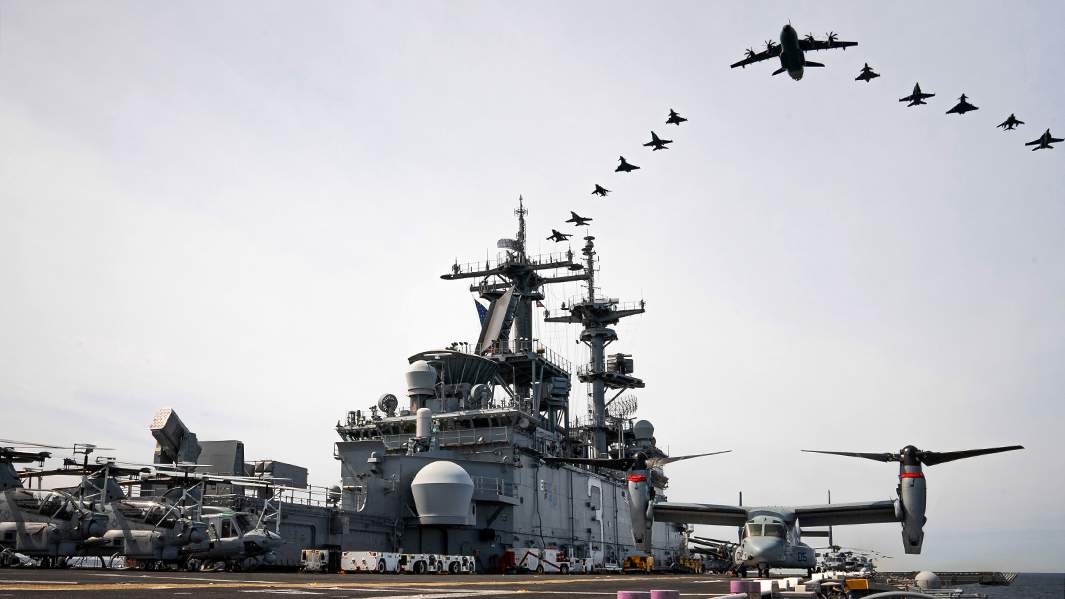 Самолеты Германии, Финляндии, Швеции и США летят строем над десантным кораблем класса Wasp USS Kearsarge во время военных учений BALTOPS 22 в Балтийском регионе, июнь 2022 года 