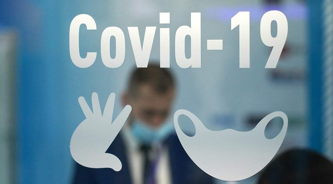 человек в медицинской маске на фоне вывески Covid-19