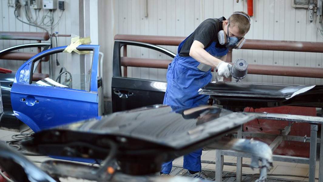 Сотрудник цеха кузовного ремонта наносит краску на поверхность детали автомобиля