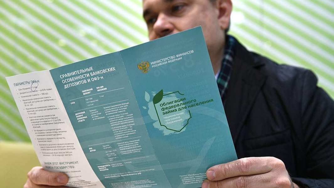 Мужчина в одном из отделений Сбербанка изучает буклет о приобретении облигаций федерального займа