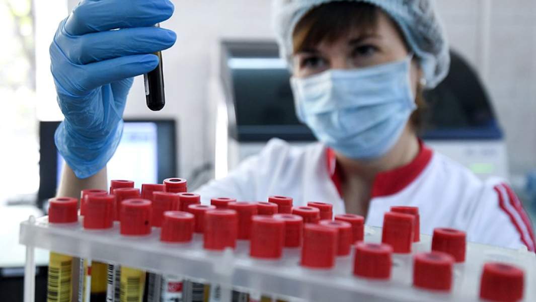 Сотрудница держит пробирки с кровью в лаборатории