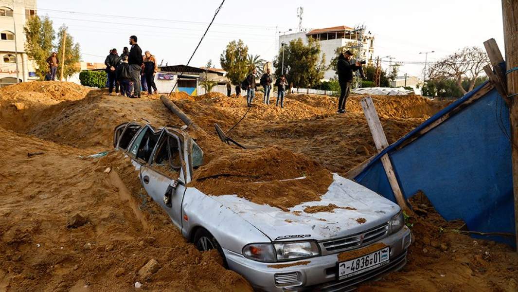Палестинцы осматривают воронку от ракеты и поврежденный автомобиль после израильских авиаударов в Газе