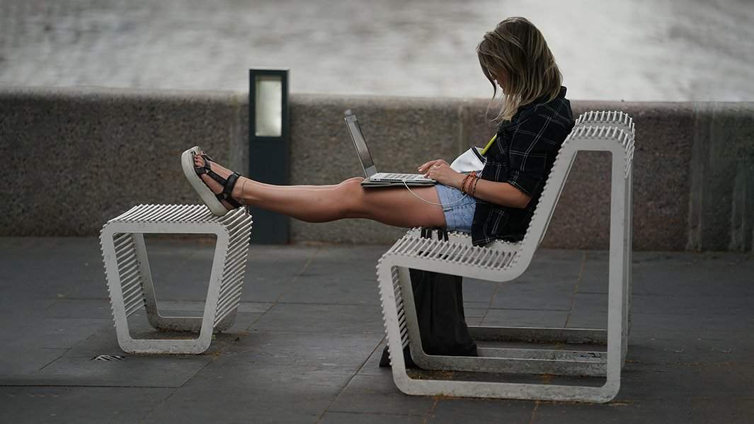 Девушка с ноутбуком на коленях на уличной скамье