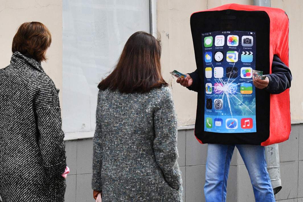 Промоутер в костюме смартфона с треснувшим экраном раздает рекламные листовки на улице