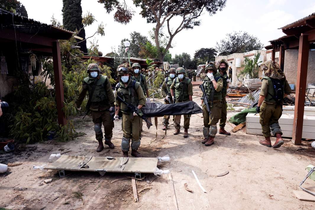 Израильские солдаты несут тело жертвы нападения боевиков ХАМАС в кибуце Кфар-Аза на юге Израиля