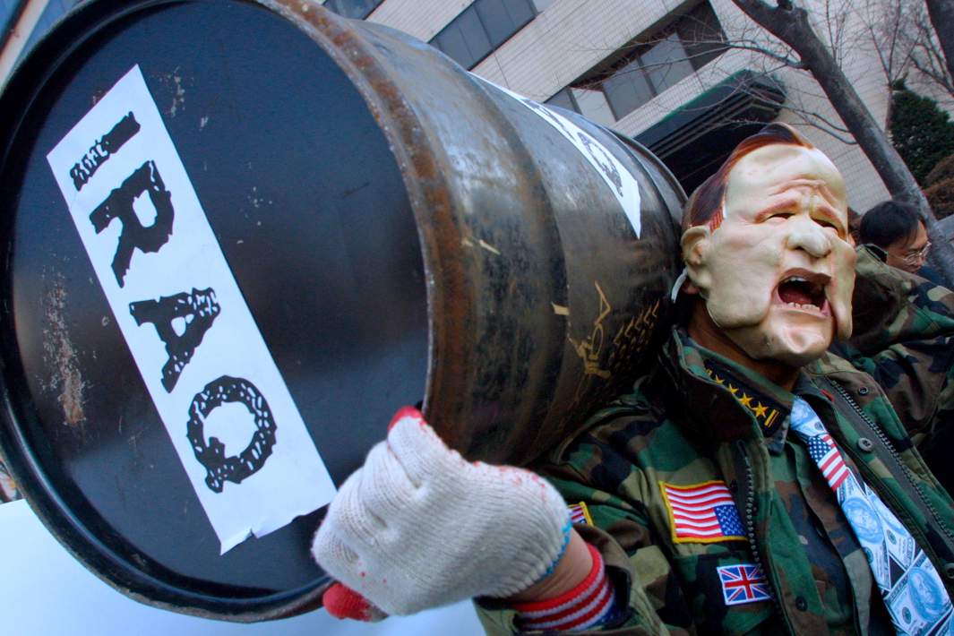 Протестующий в маске, изображающей президента США Джорджа Буша, держит бочку с нефтью на антивоенном митинге возле посольства США в Сеуле. 14 февраля 2003 года