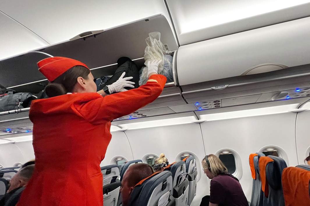 Бортпроводница помогает уложить багаж на полках в самолете