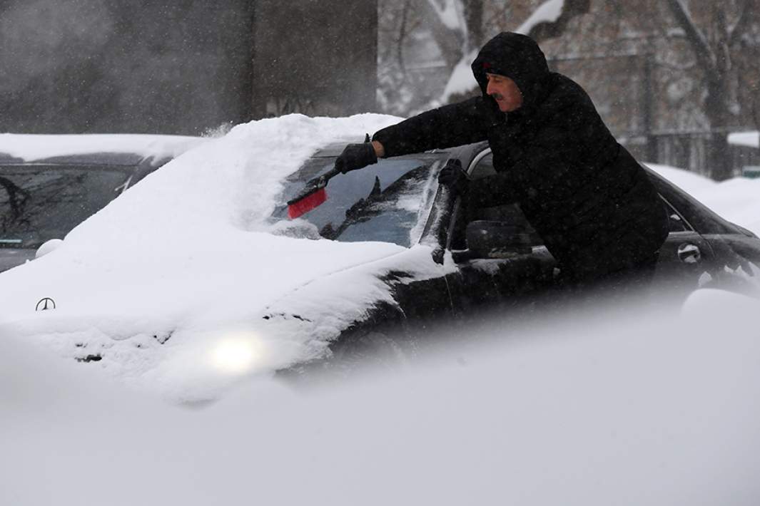 Мужчина чистит машину от снега