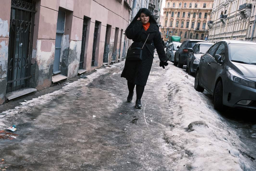 Пешеход идет по льду на тротуаре