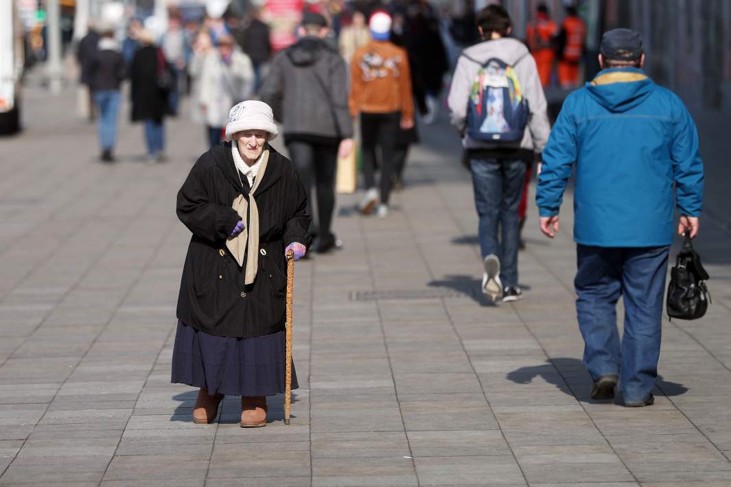 пожилая женщина идет по улице с тростью светит солнце