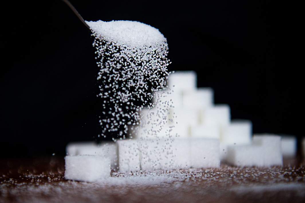 Сахар сыпется с ложки на фоне кубиков сахара