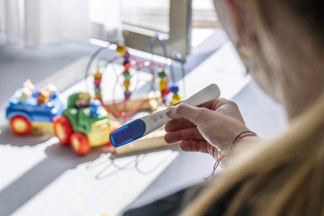 девушка держит положительный тест на береенность на фоне детских игрушек