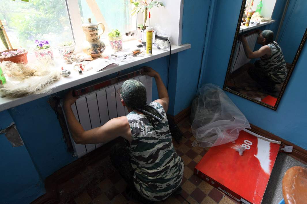 Рабочий устанавливает радиатор отопления в подъезде жилого дома