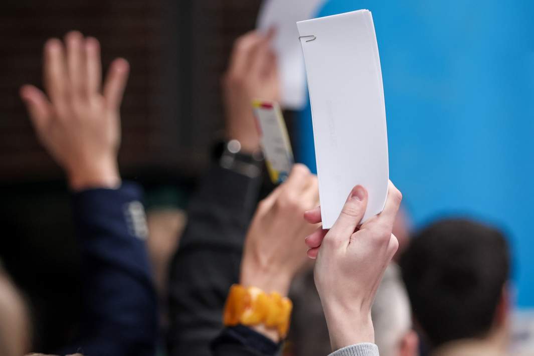 люди поднимают руки с листками для голосования