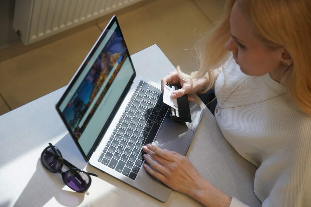 Девушка совершает покупку в интернете, держит банковскую карту в руках и смотрит в ноутбук