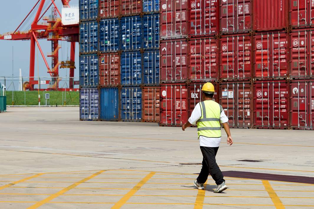 Рабочий идет на порте по доставке контейнеров с товарами из Китая