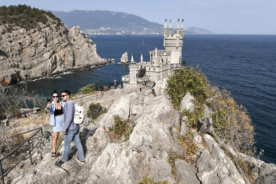 Туристы фотографируются у замка «Ласточкино гнездо» на береговой скале в поселке Гаспра в Крыму