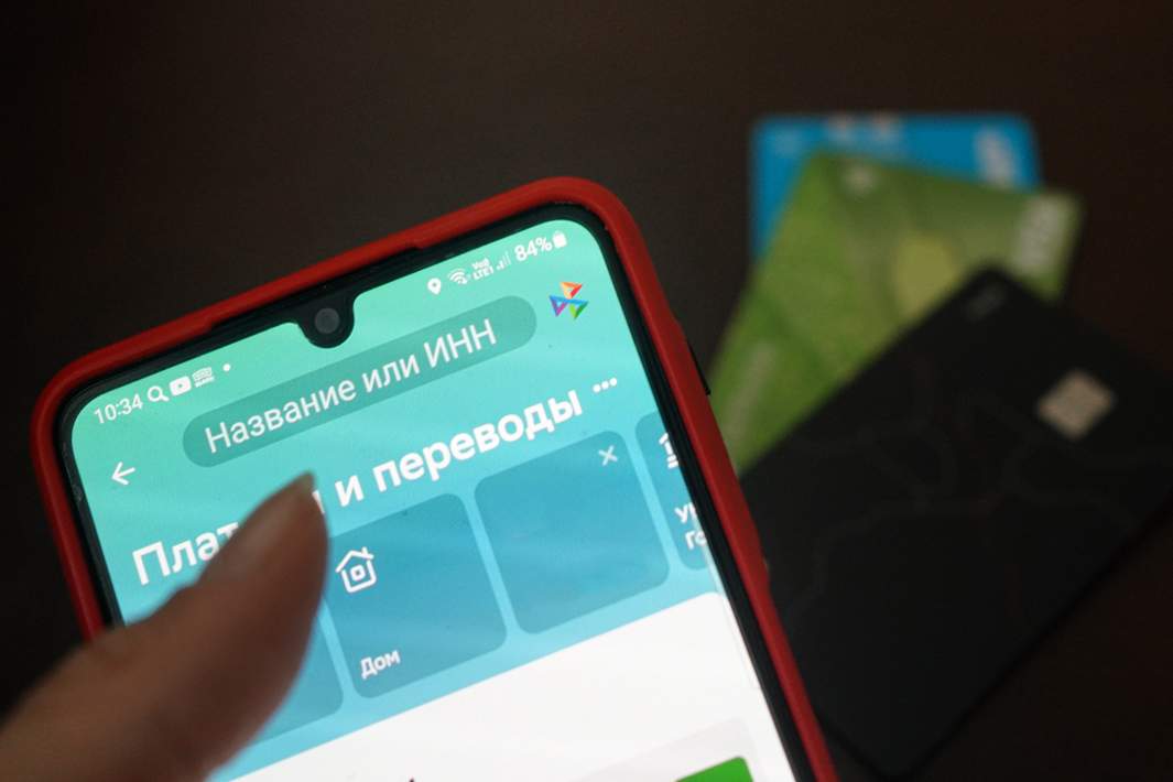 Экран телефона с приложением системы быстрых переводов на фоне банковских карт