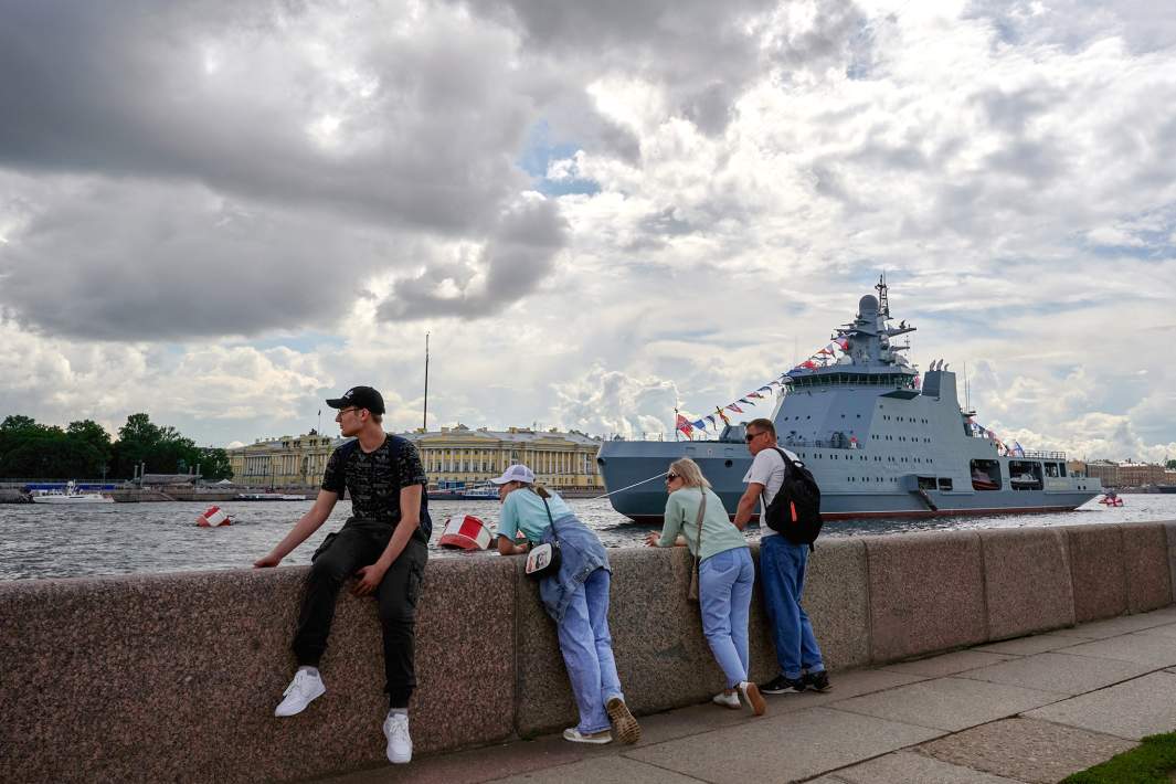 Зрители на набережной смотрят на проход кораблей в акватории Невы в преддверии Дня ВМФ в Санкт-Петербурге. На втором плане: патрульный корабль ледового класса «Иван Папанин» проекта 23550