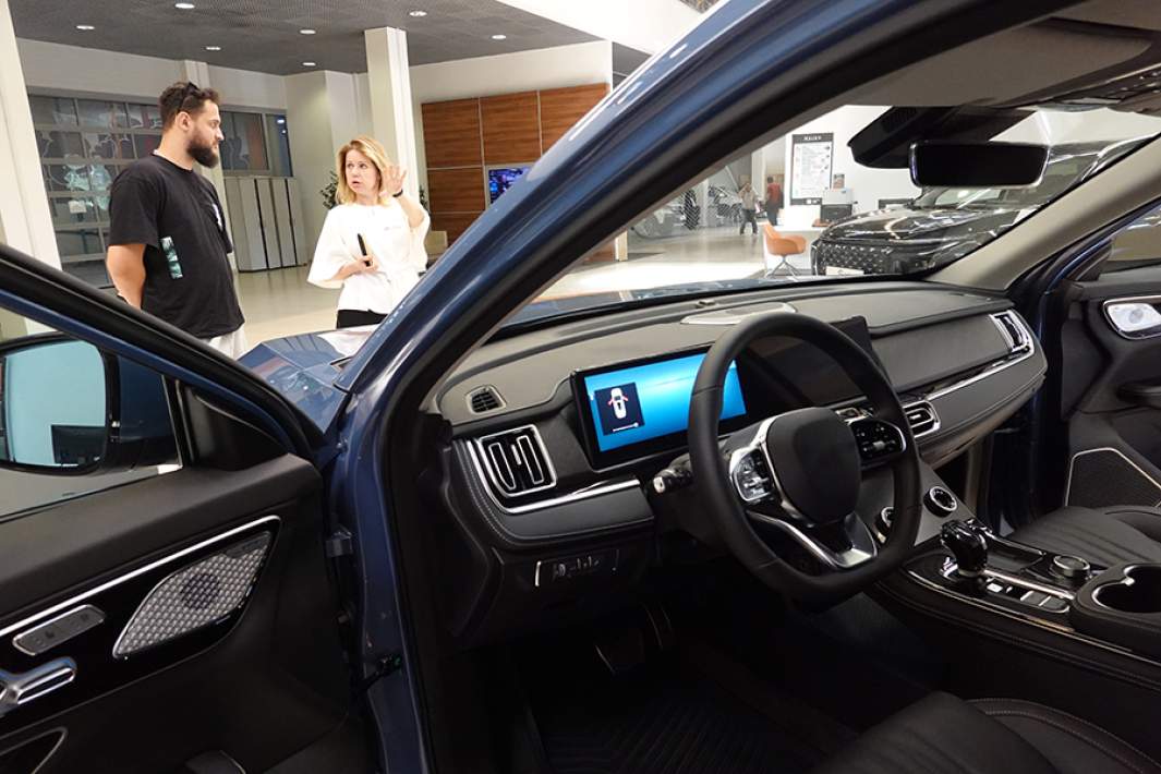 Посетитель беседует с менеджером отдела продаж около нового автомобиля 