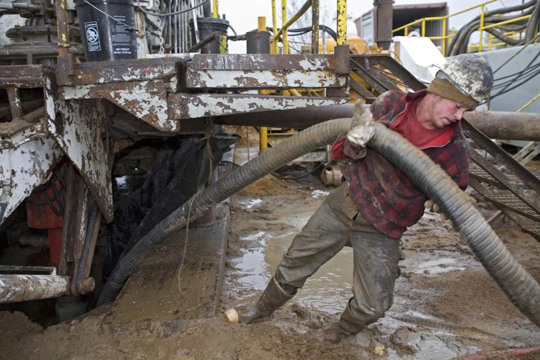 Рабочий борется со шлангом во время демонтажа буровой установки