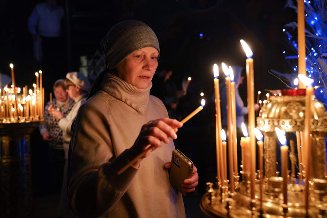 Женщина ставит свечу в храме 