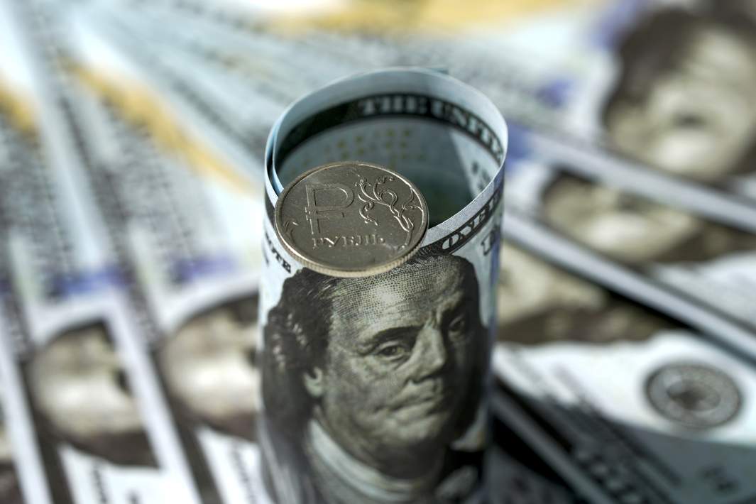 Монета номиналом один рубль на фоне стодолларовых купюр