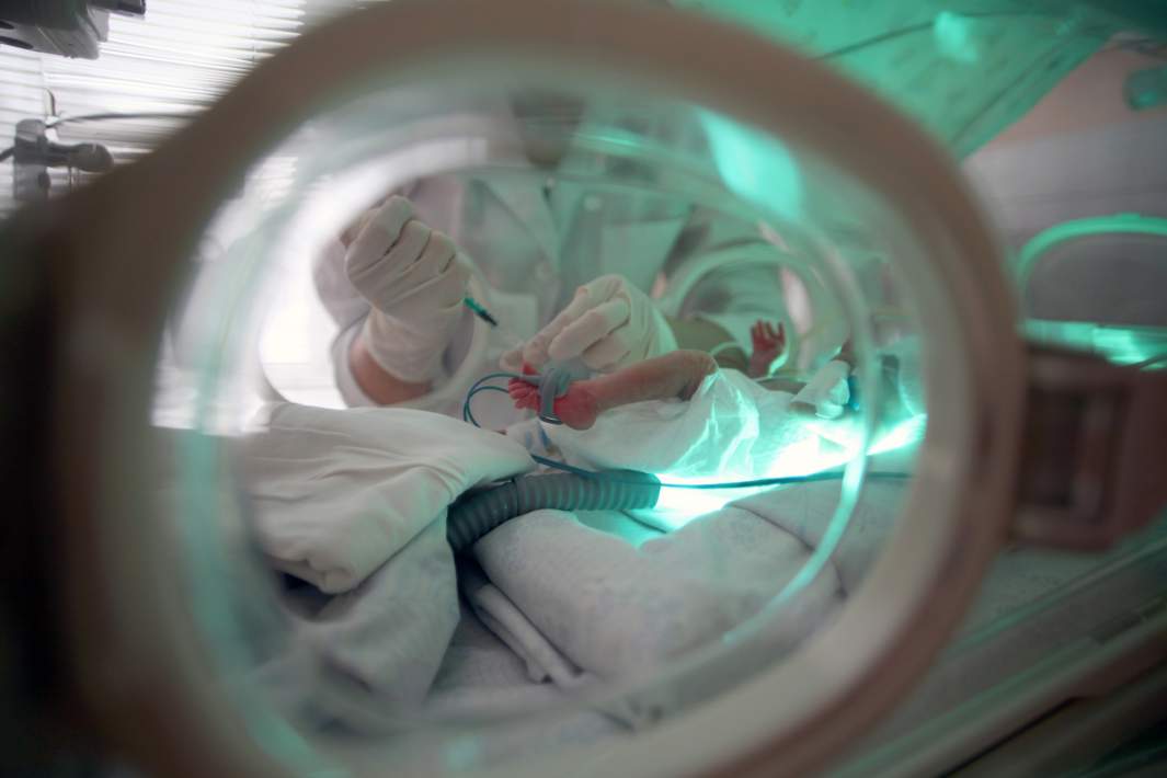 Медицинская сестра производит внутривенное введение лекарственных препаратов ребенку в отделении реанимации новорожденных