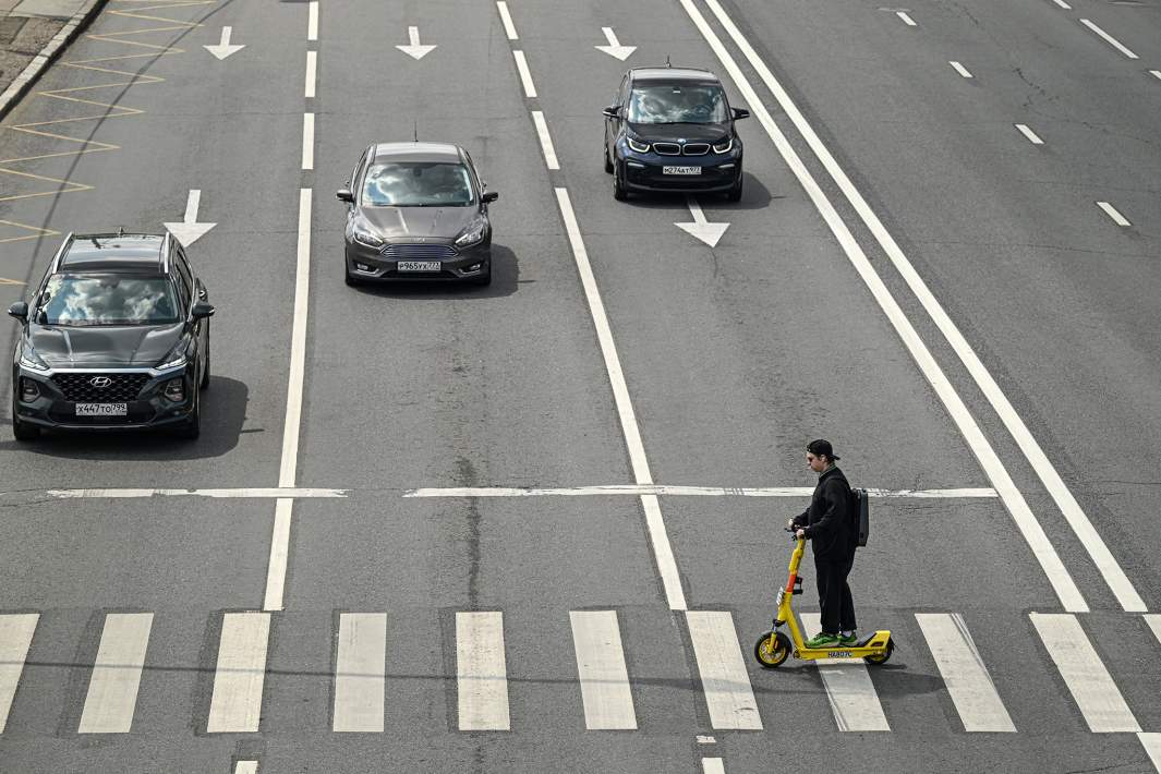 Молодой человек едет на самокате по пешеходному переходу