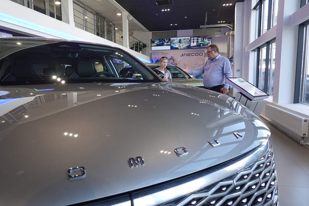 Менеджер отдела продаж китайских автомобилей консультирует покупательницу около автомобилей