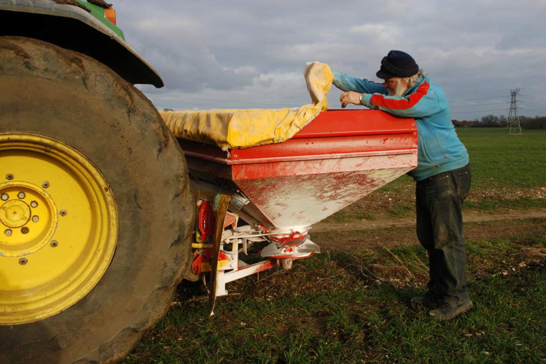 Работник фермы осматривает разбрасыватель удобрений