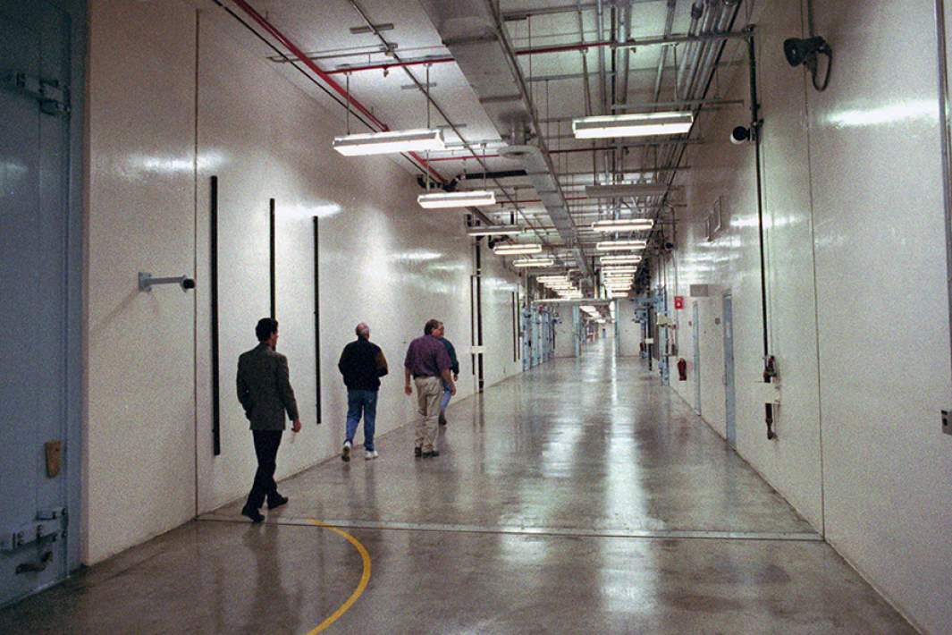 Группа людей идет по коридору, который петляет через сборочный це устройств, в котором размещается 30 отдельных зданий на испытательном полигоне Невады в Меркьюри, штат Невада. 1997 год 