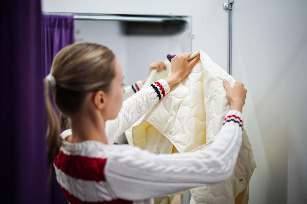 Женщина смотрит на куртку в примерочной