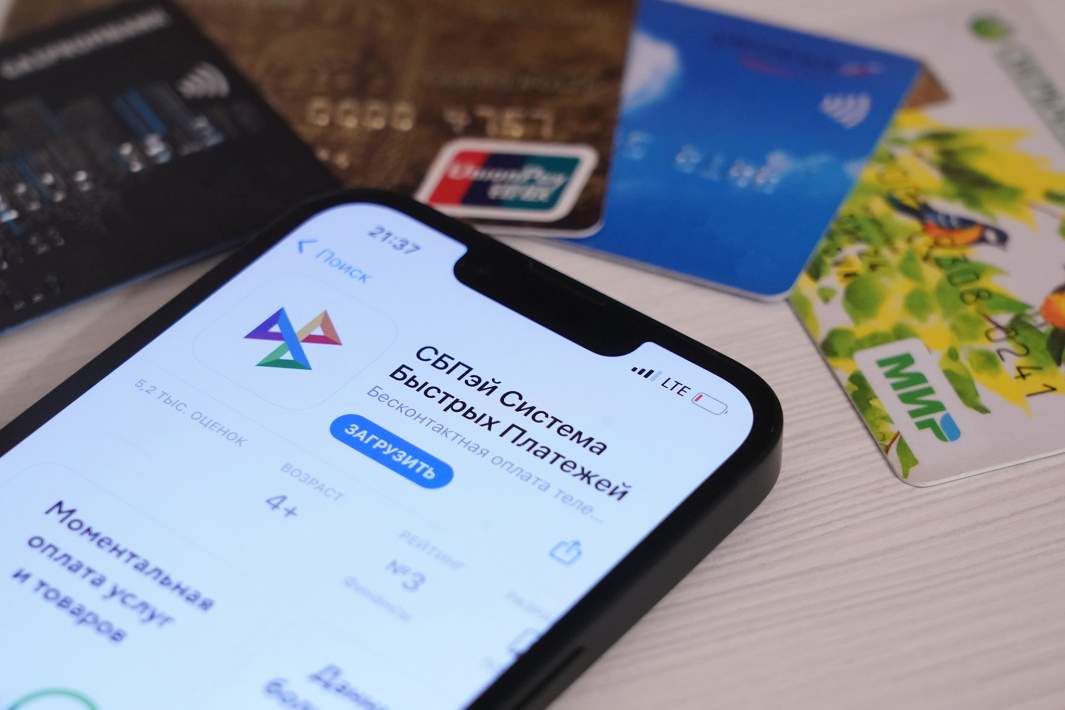 Экран телефона с приложением системы быстрых платежей «СБПэй» на фоне банковских карт