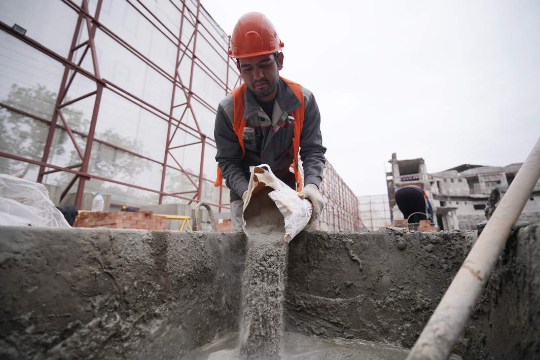 Рабочий засыпает цемент 