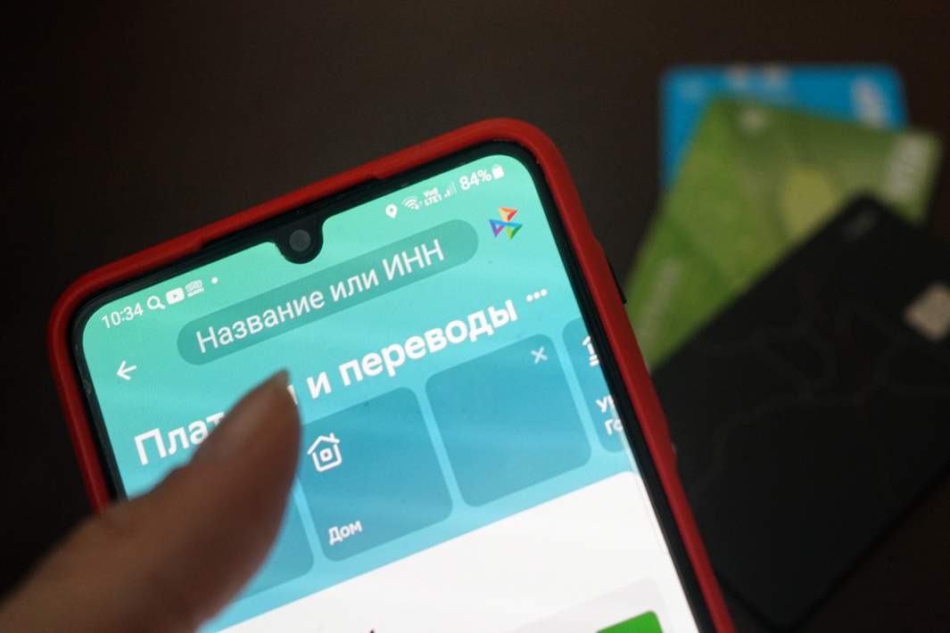 Экран телефона с приложением системы быстрых переводов на фоне банковских карт