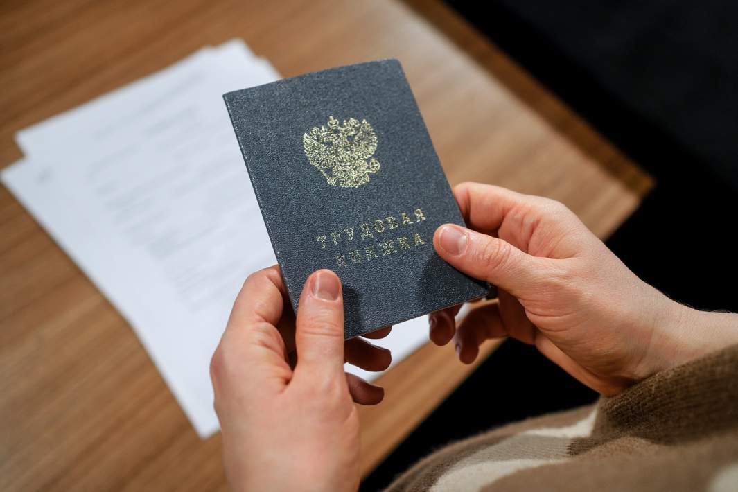 Трудовая книжка в руках и трудовой договор на столе