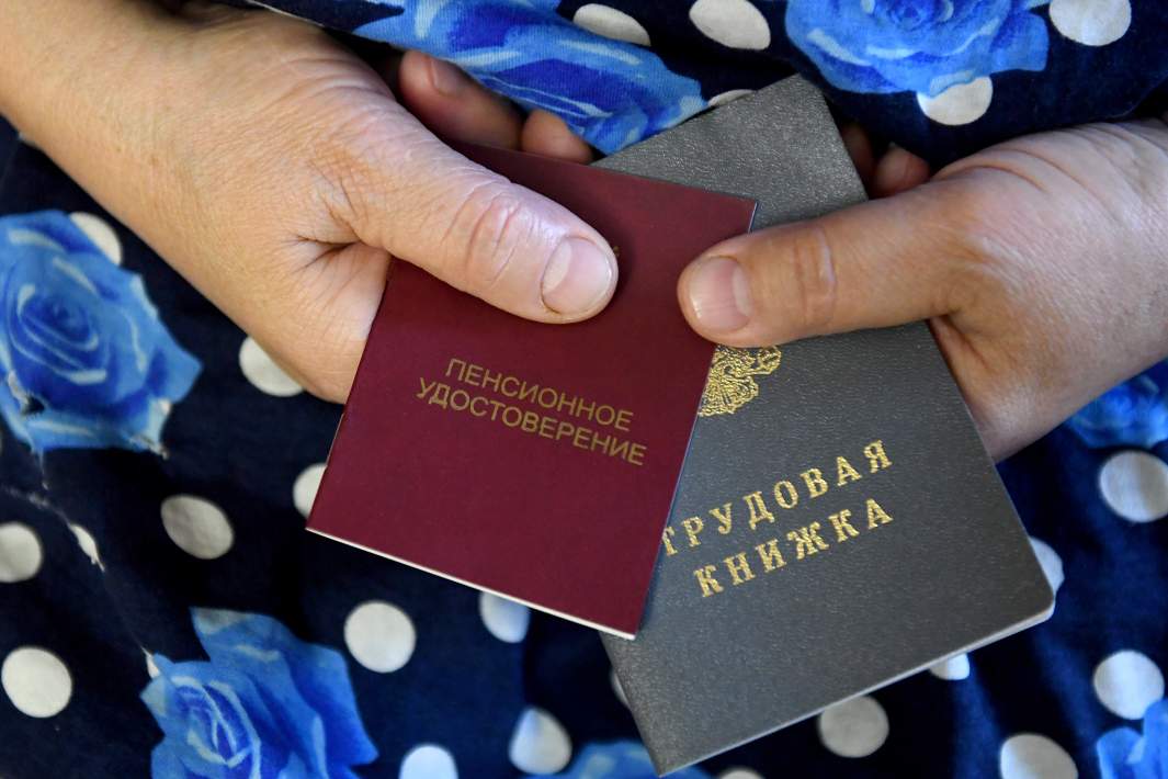 Пенсионерка держит трудовую книжку и пенсионное удостоверение